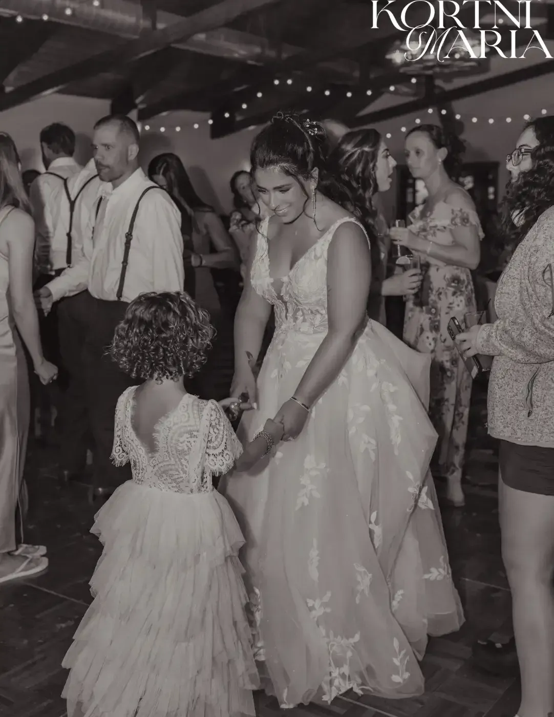 A bride and her flower girl are dancing at a wedding reception