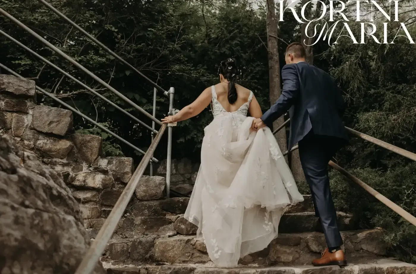 A bride and groom are walking up a set of stairs holding hands.