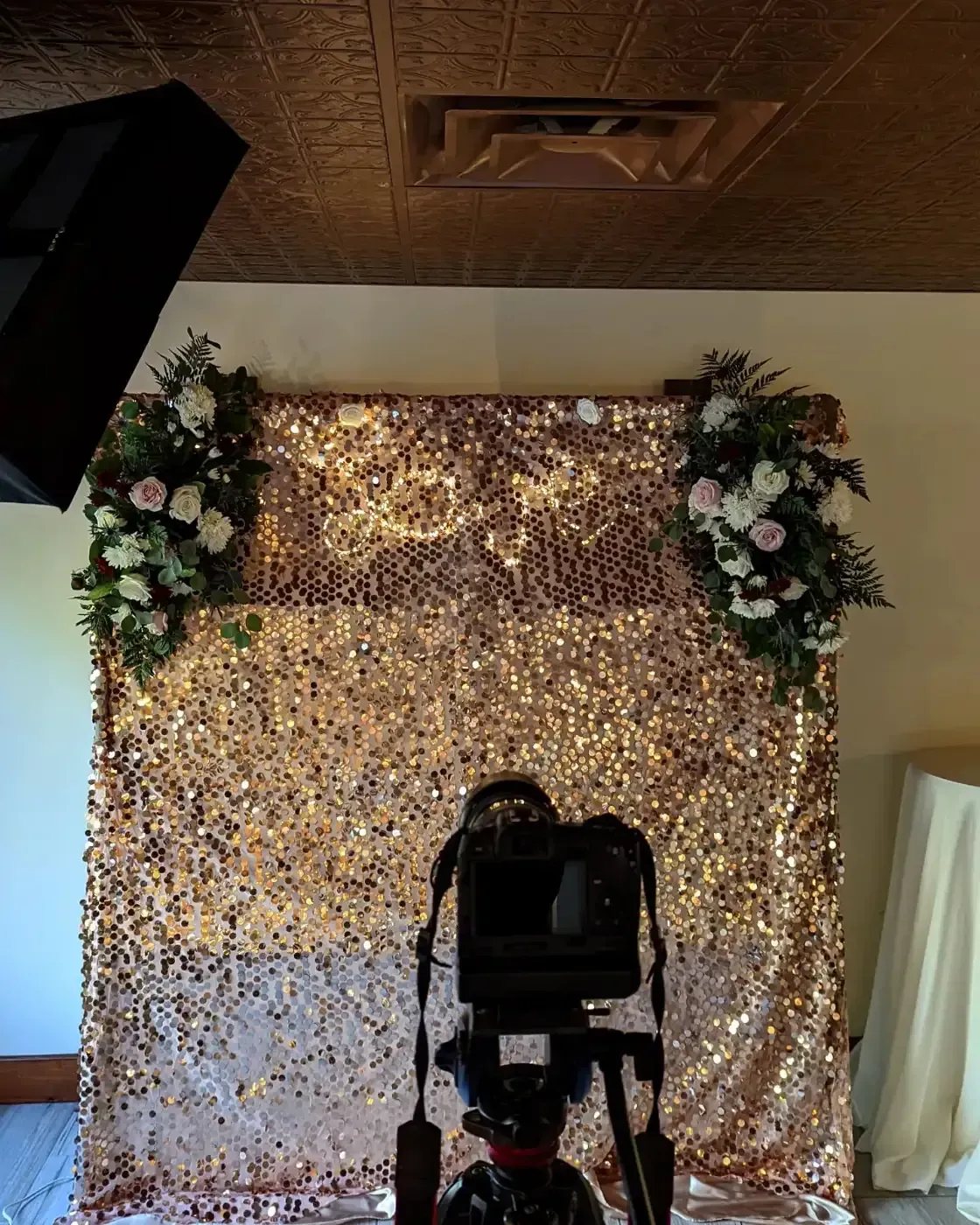A camera is sitting in front of a gold sequined backdrop.