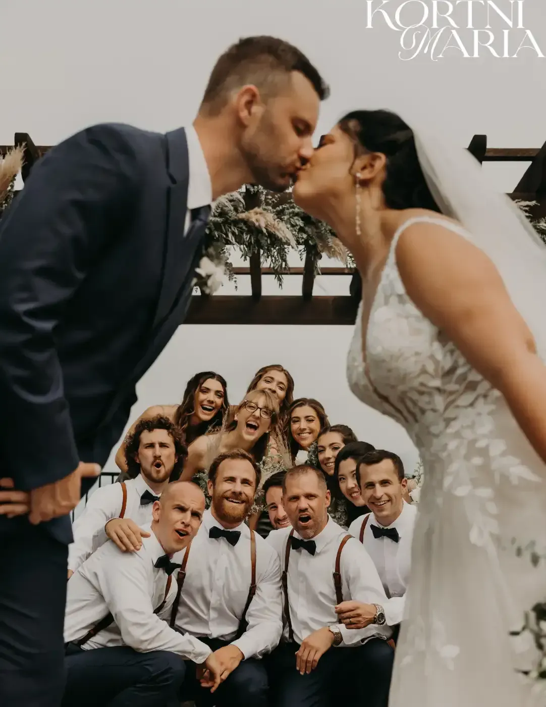 A bride and groom kissing in front of their wedding party