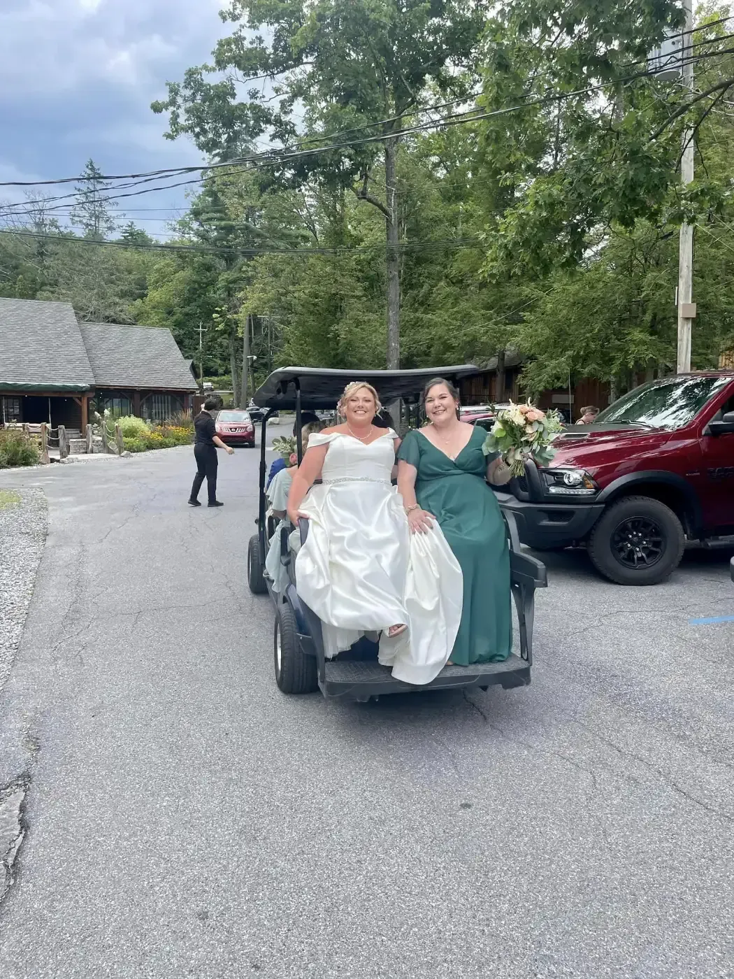 A bride and her bridesmaid are riding in a golf cart.