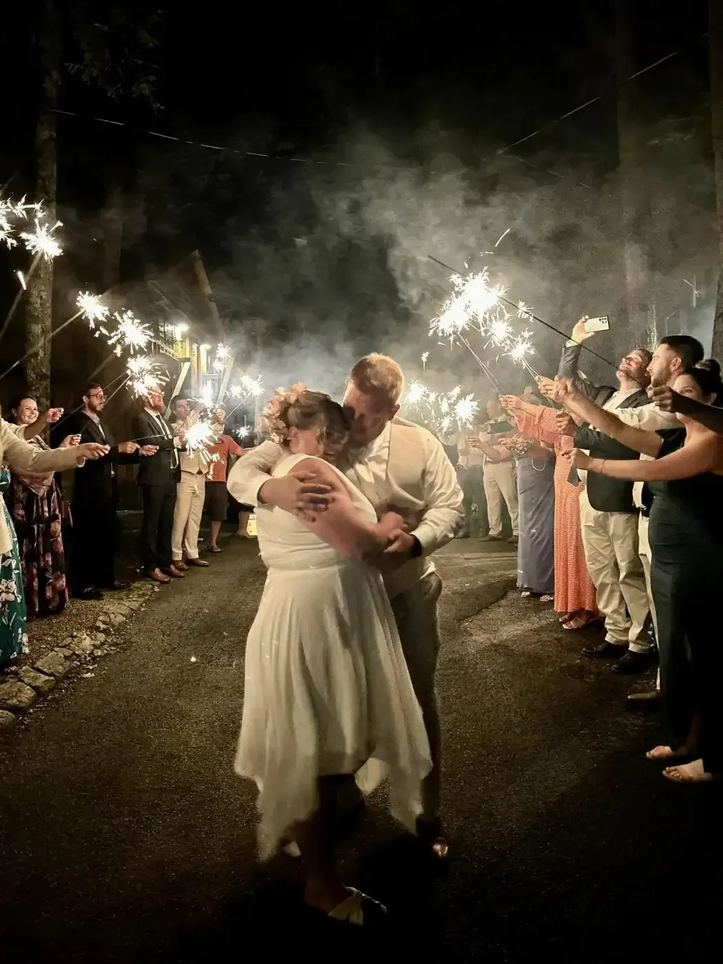 A bride and groom are dancing in front of a crowd of people holding sparklers.
