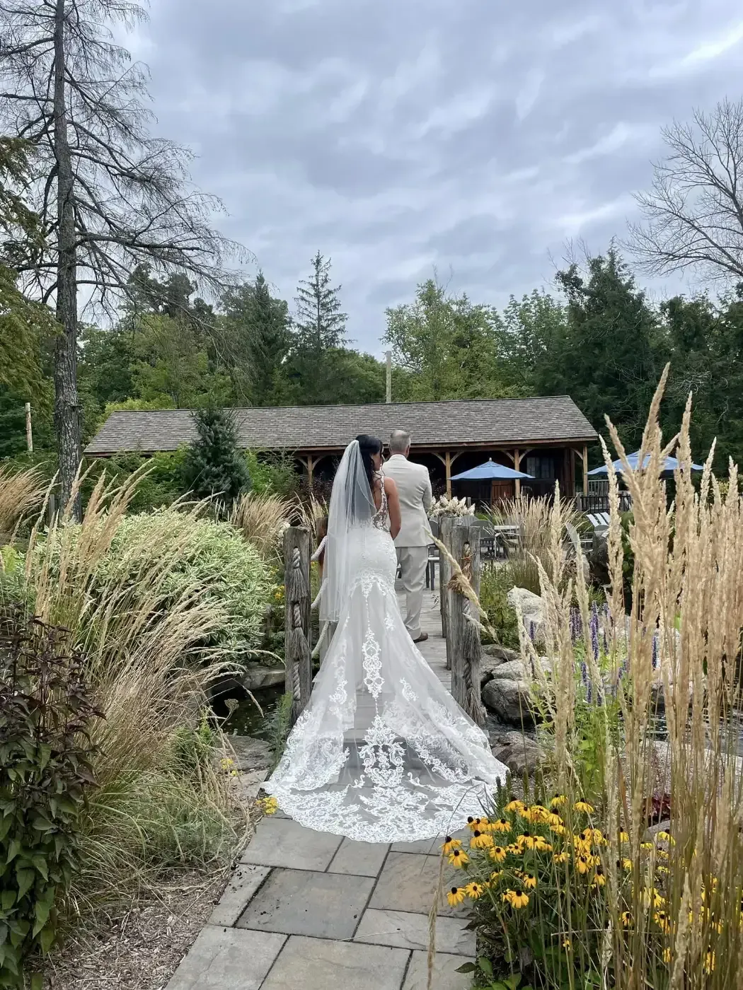 A bride and groom are standing on a bridge in a garden.