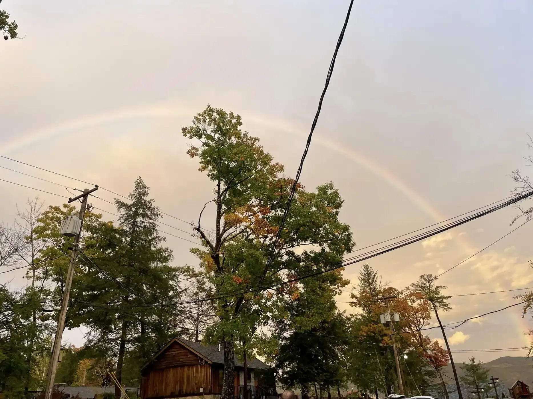 A rainbow is visible in the sky over a house and trees.