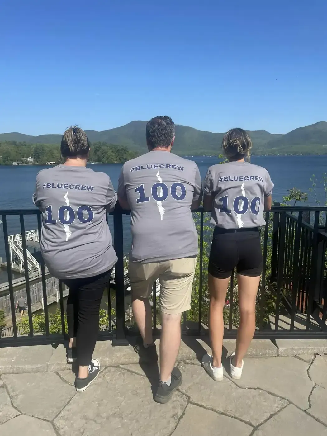 Three people are standing on a balcony overlooking a lake.