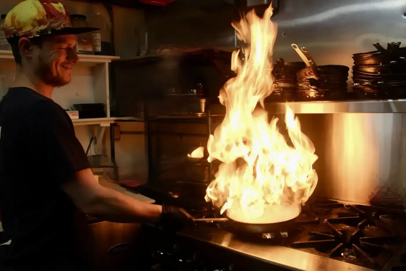 A man is cooking food in a frying pan with flames coming out of it.