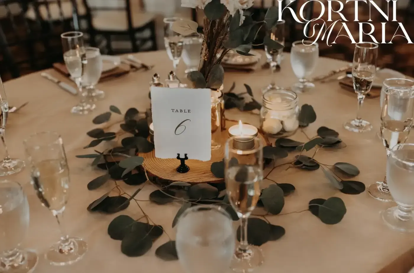 A table set for a wedding reception with a wooden centerpiece surrounded by leaves and candles.