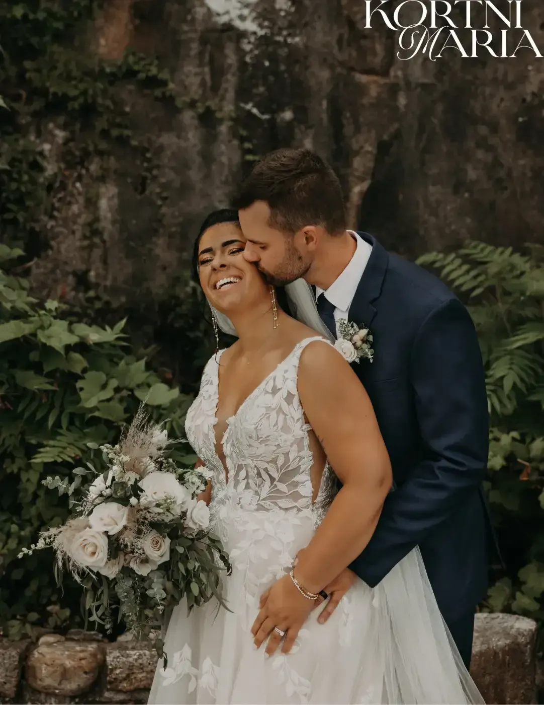 A bride and groom are kissing in front of a waterfall.