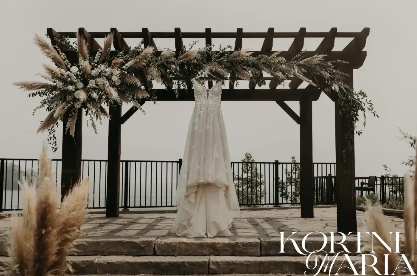 A wedding dress is hanging under a pergola with flowers.