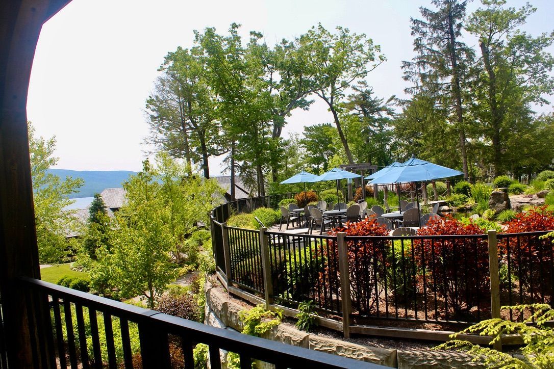 A balcony overlooking a lush green garden with tables and umbrellas.