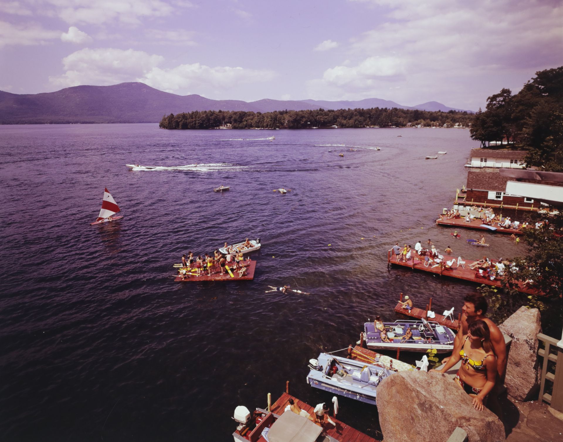 A couple standing on a rock overlooking the lake with boats in it