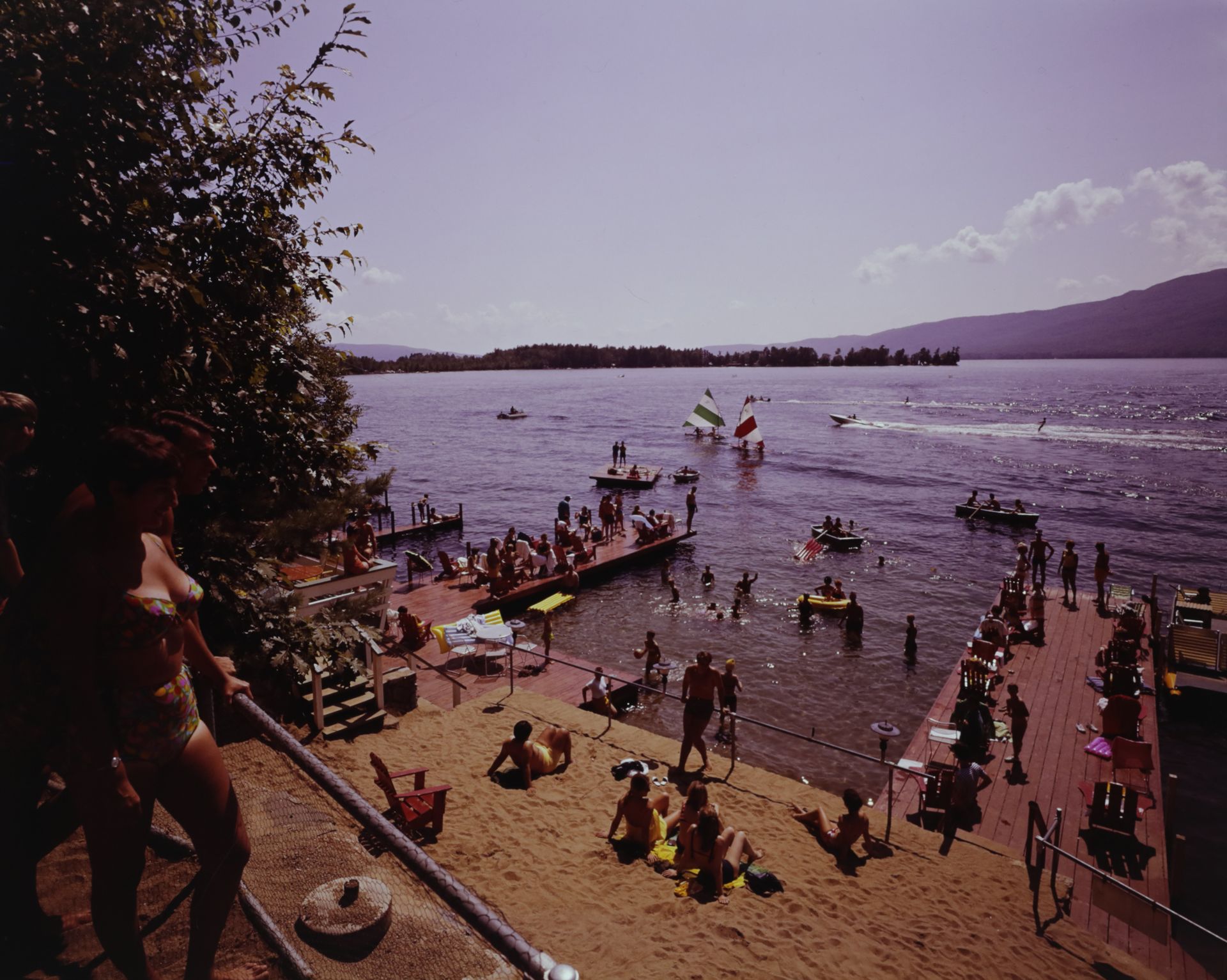 A group of people are gathered on a beach near Lake George