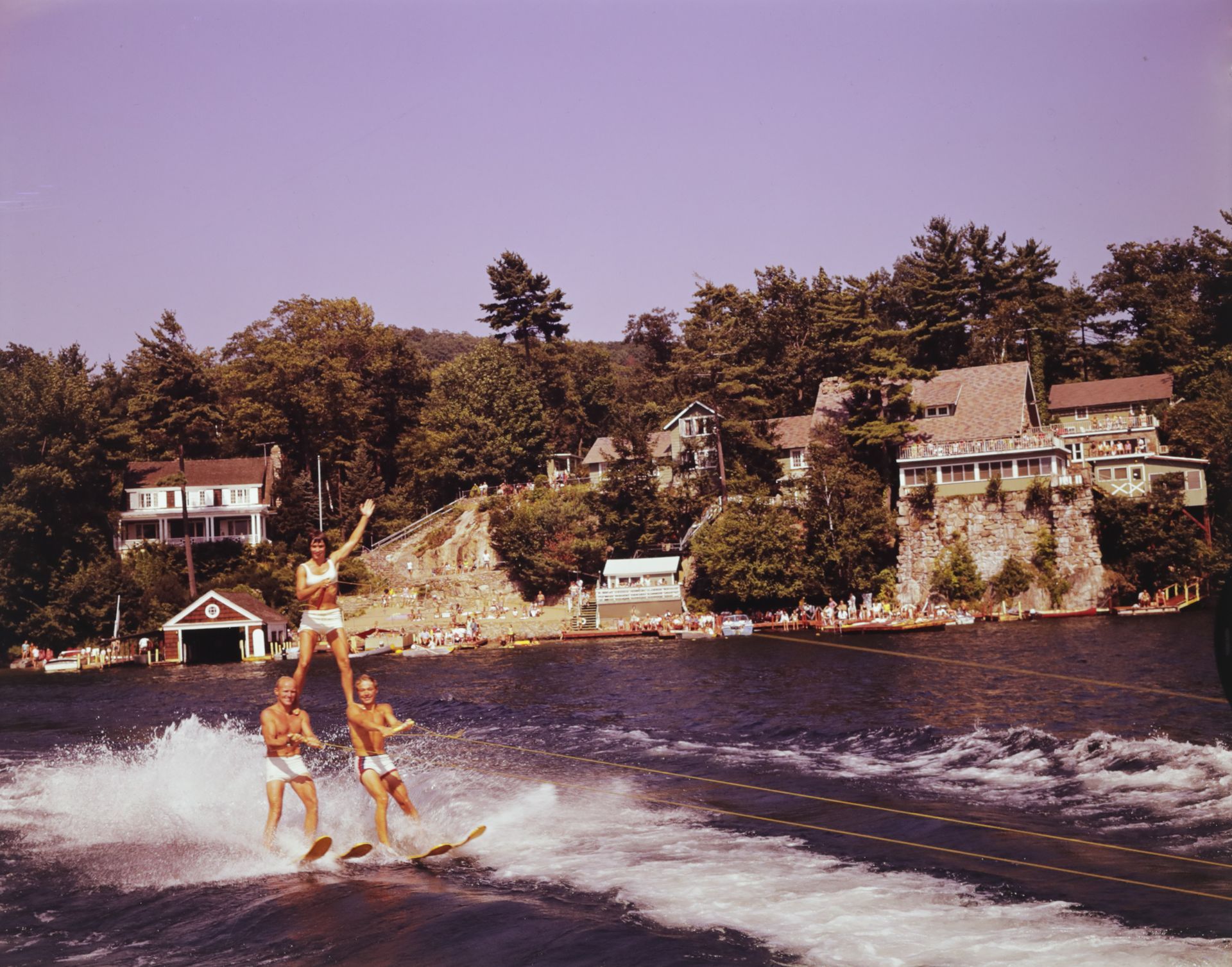 A group of people are water skiing on a lake in front of Blue Water Manor