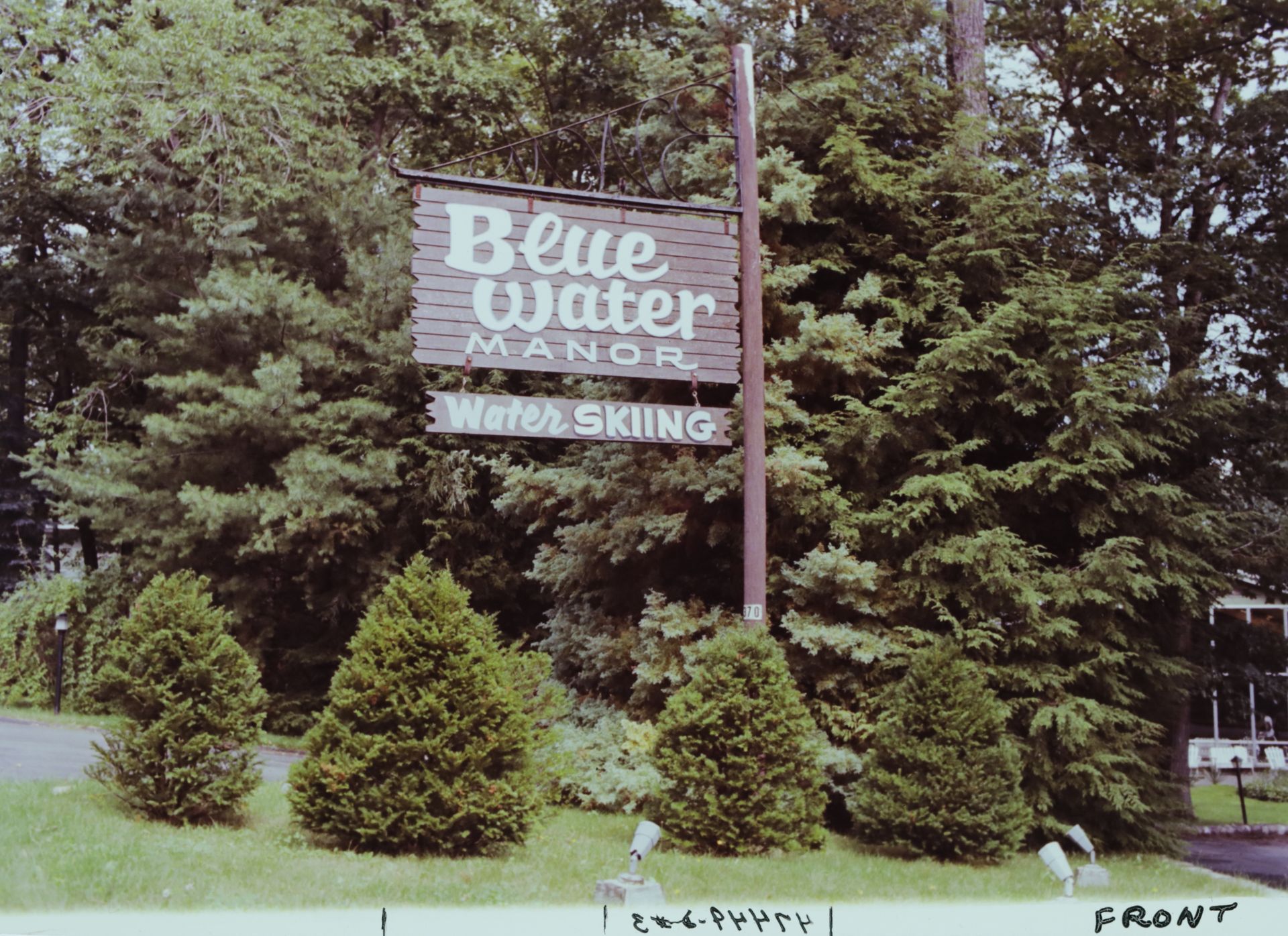 A sign for Blue Water Manor is surrounded by trees