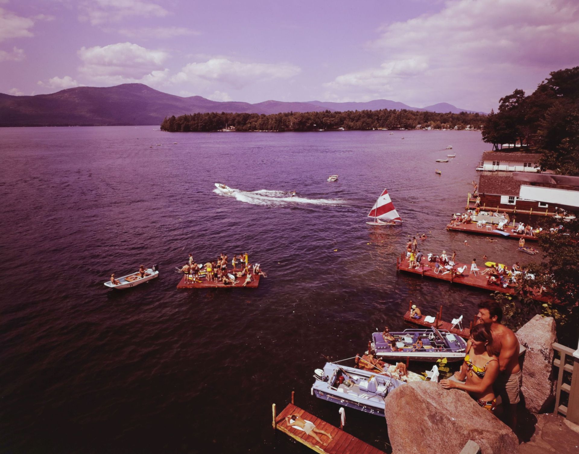 A couple standing on a rock overlooking a lake with boats in it