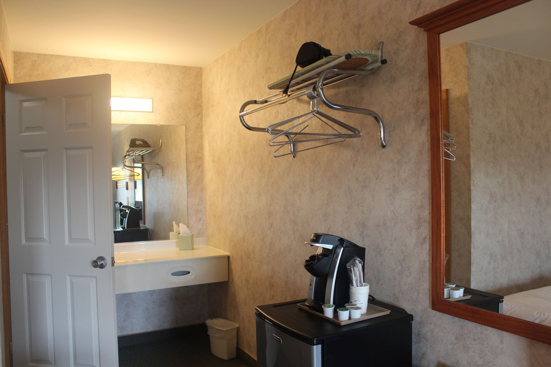 A hotel room with a sink , mirror and coffee maker.