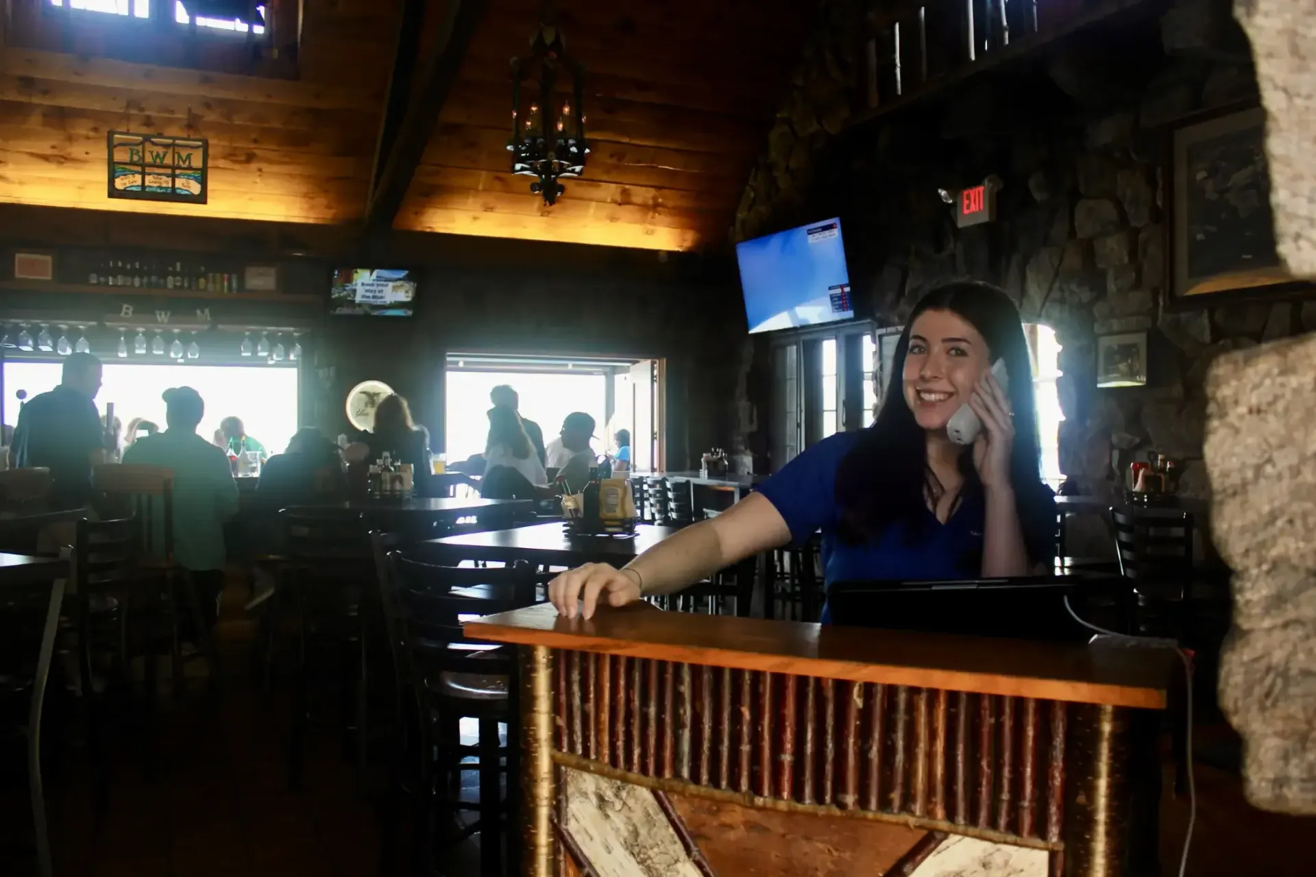 A woman is sitting at a counter in a restaurant talking on a cell phone.