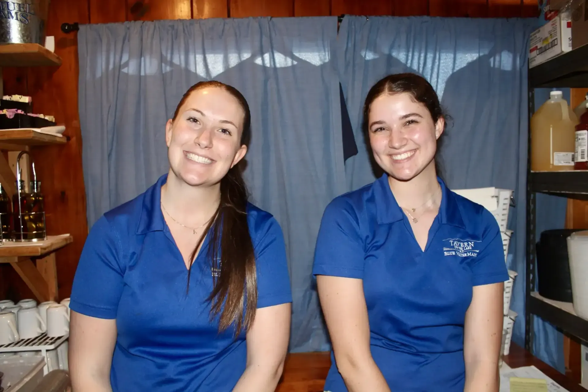 Two women in blue shirts are sitting next to each other and smiling