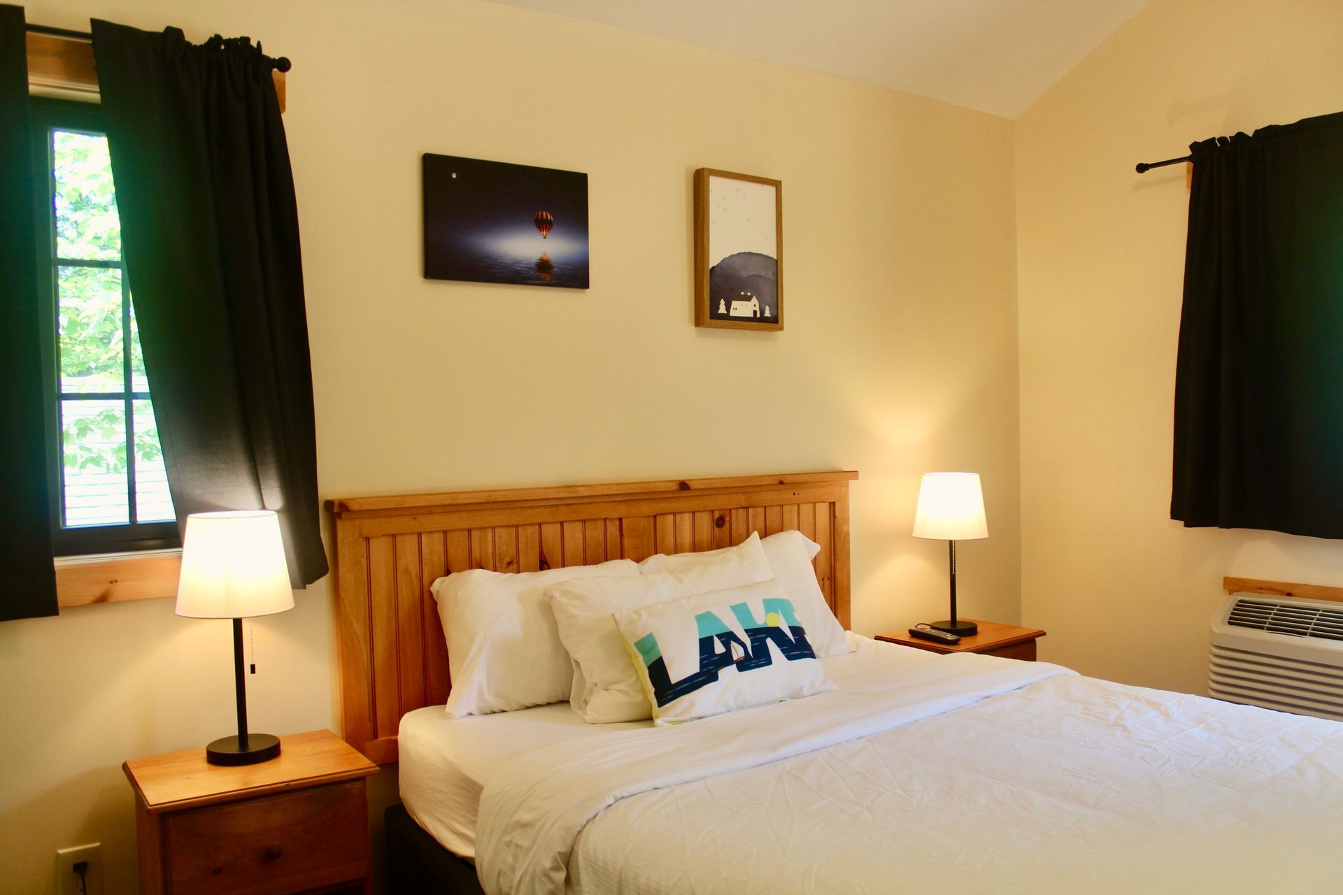 A bedroom with a bed , nightstand , lamp and two windows.