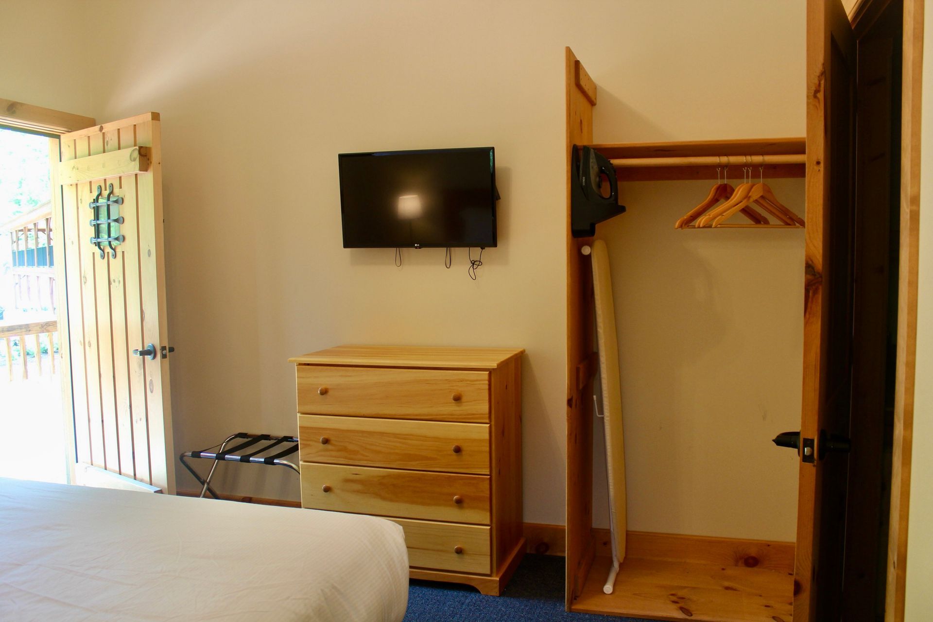 A hotel room with a bed , dresser , television and closet.