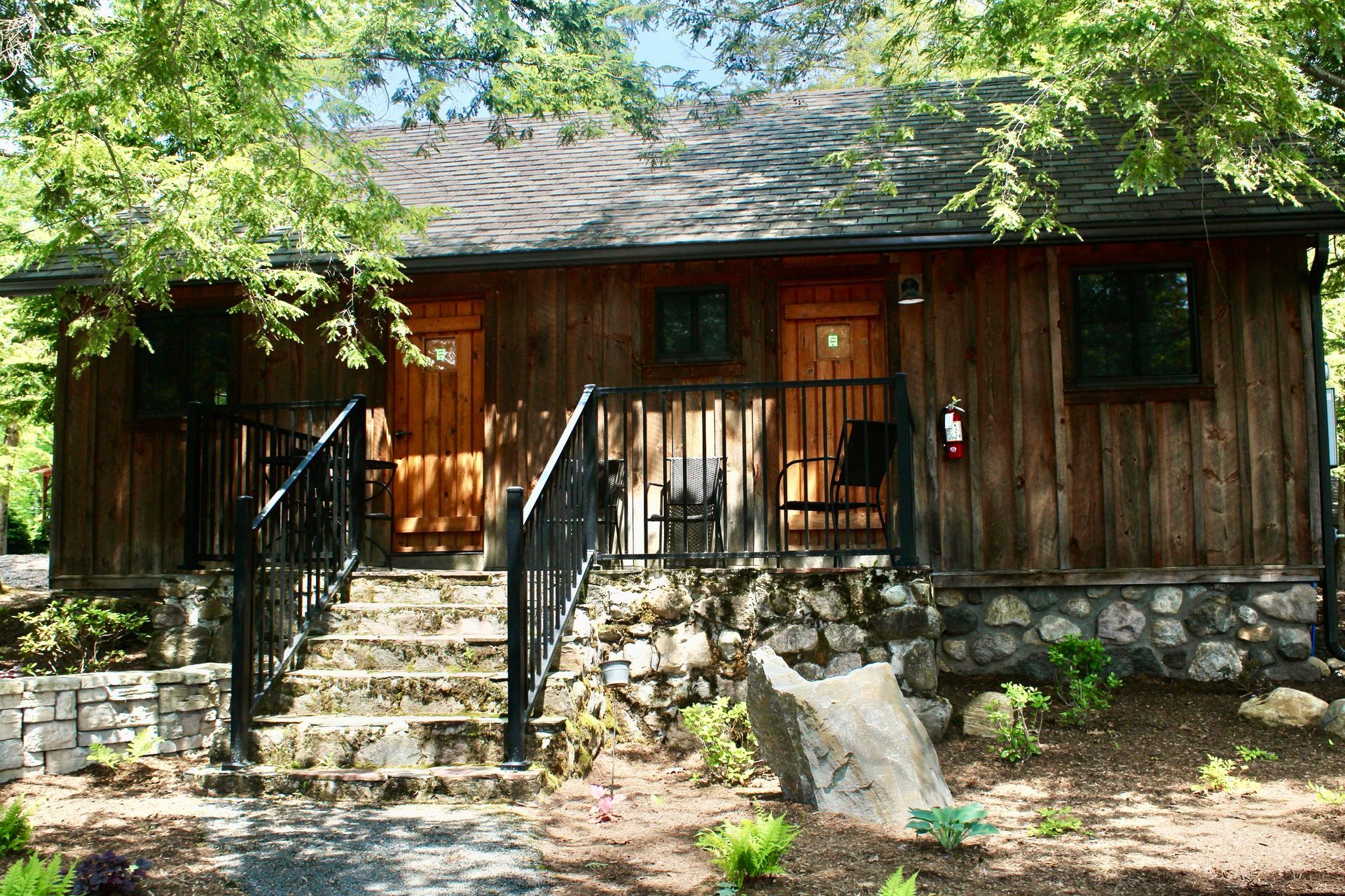 A small wooden house with stairs leading up to it is surrounded by trees.