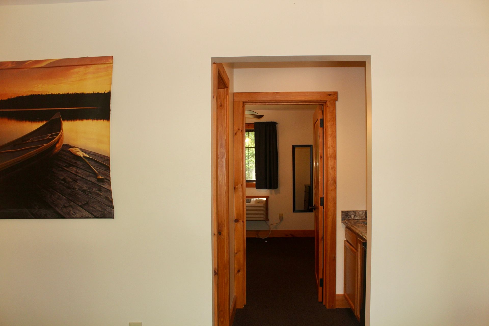 A room with a picture of a boat on the wall and a doorway leading to another room.