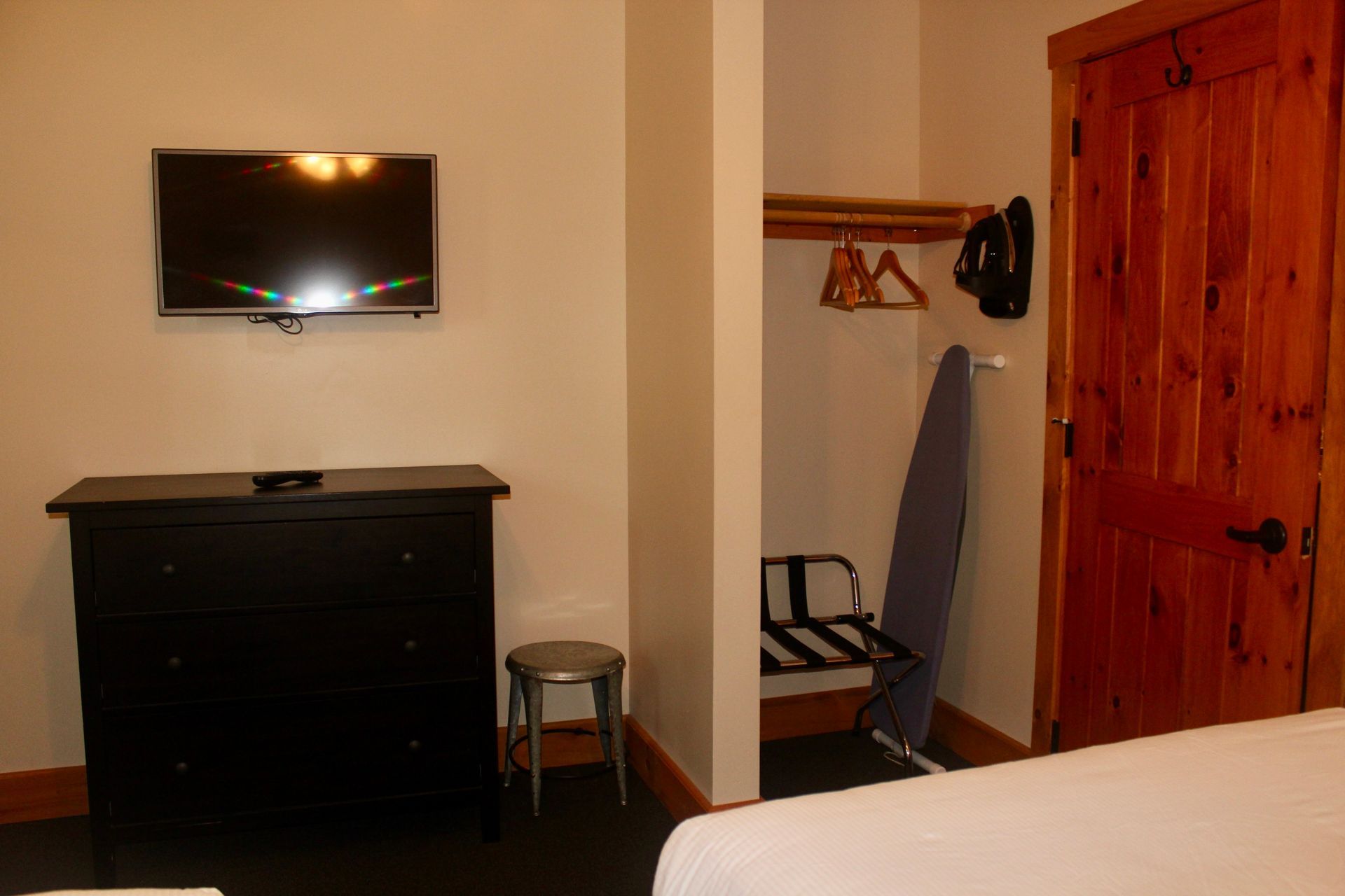 A bedroom with a bed , dresser , television and ironing board.