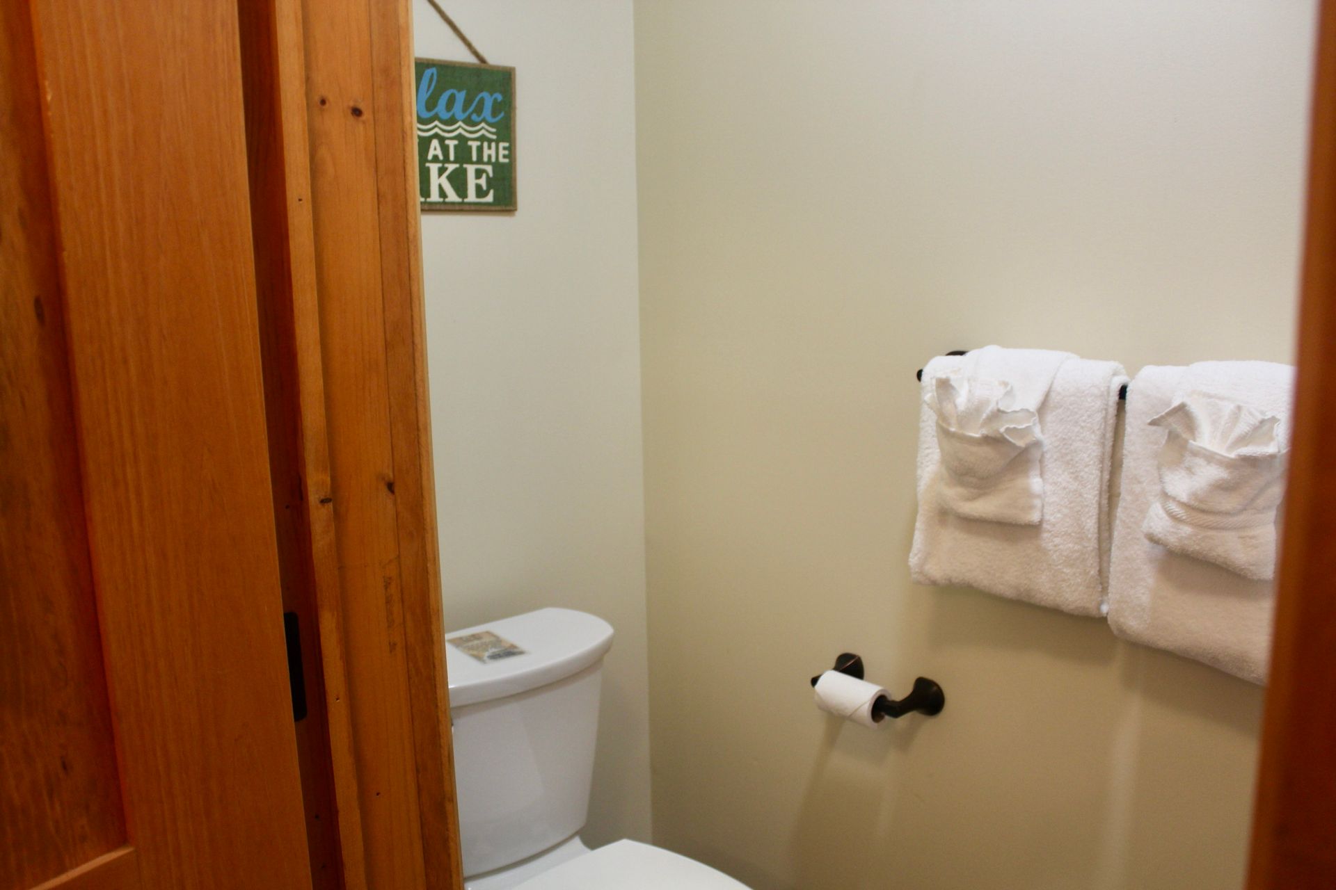 A bathroom with a toilet , towels and a sign on the wall.