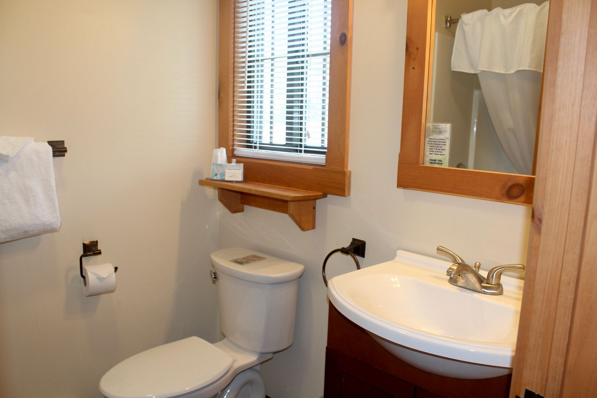A bathroom with a toilet , sink , mirror and window.