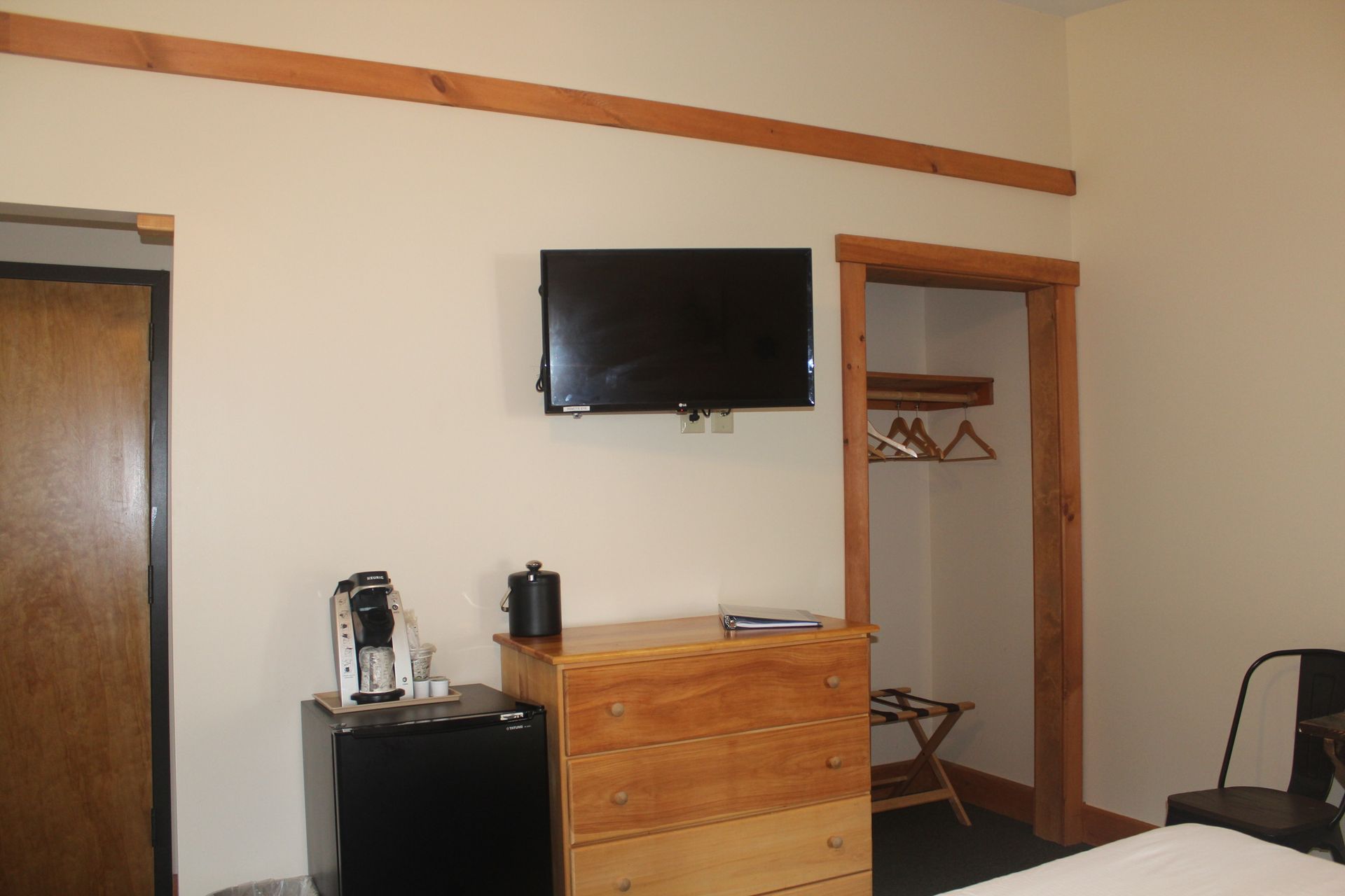 A hotel room with a bed , dresser , refrigerator and television.