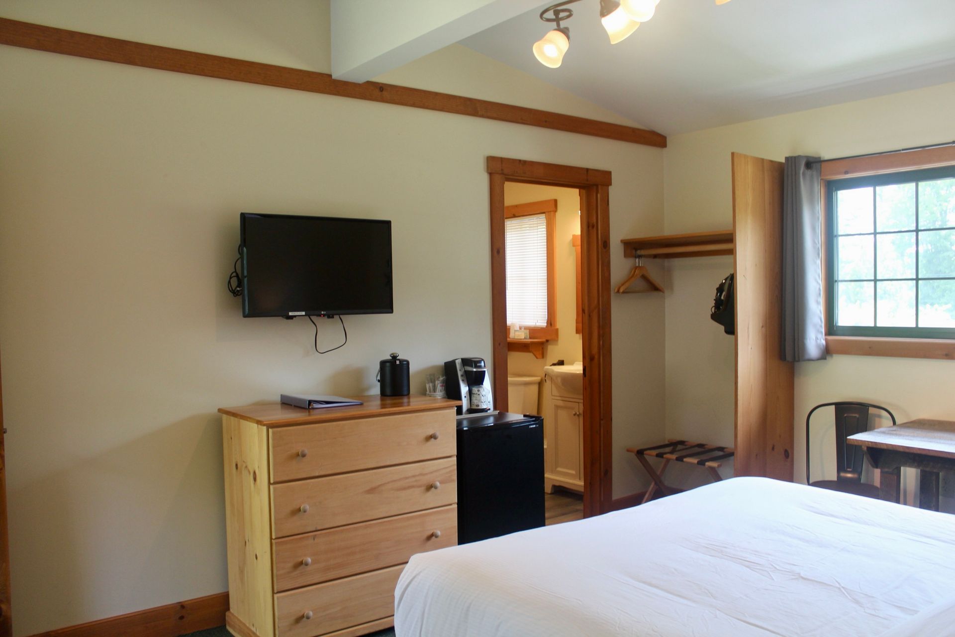 A hotel room with a bed , dresser , television and refrigerator.