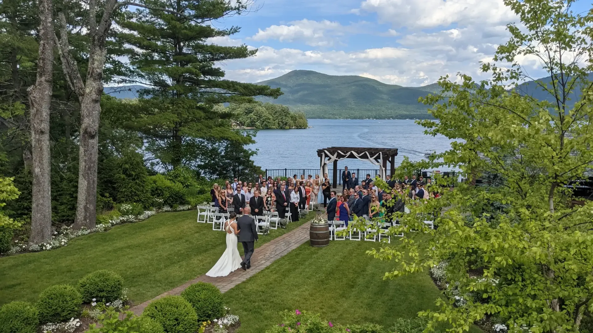 A bride and groom are walking down the aisle at their wedding ceremony in front of a lake.
