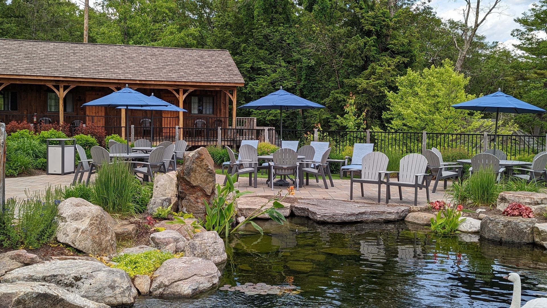There is a pond in the middle of the garden with tables and chairs and umbrellas.