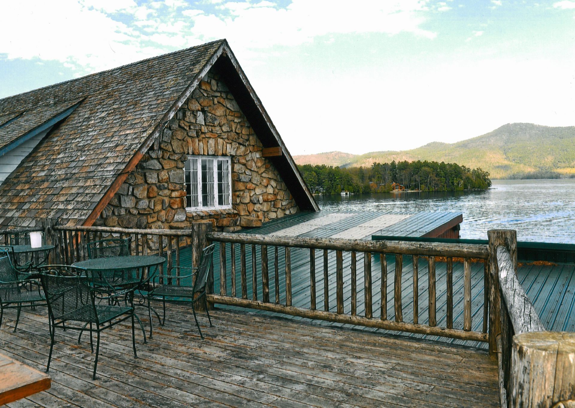 A wooden deck with tables and chairs overlooking a lake.