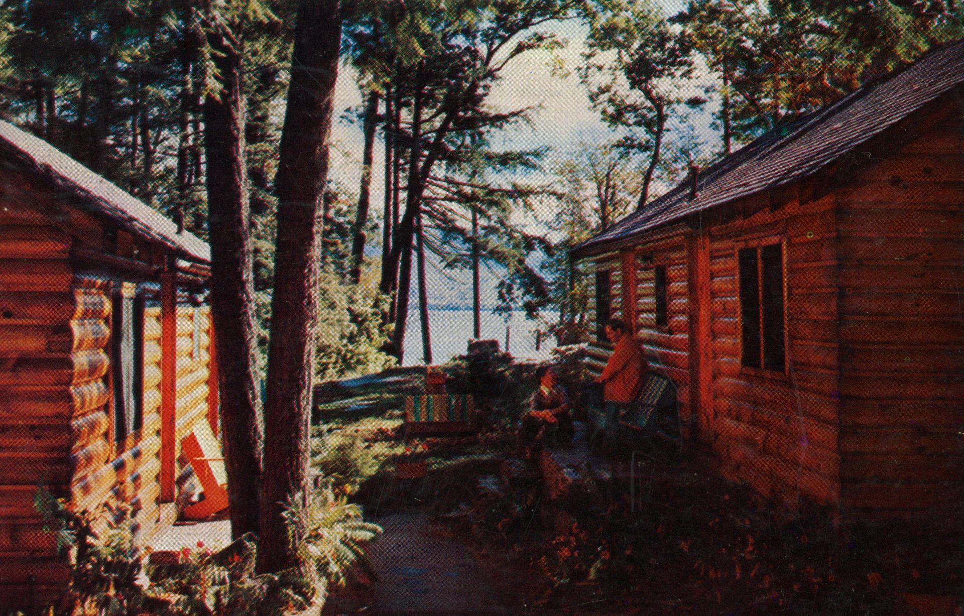 A man sits on a porch in front of a log cabin