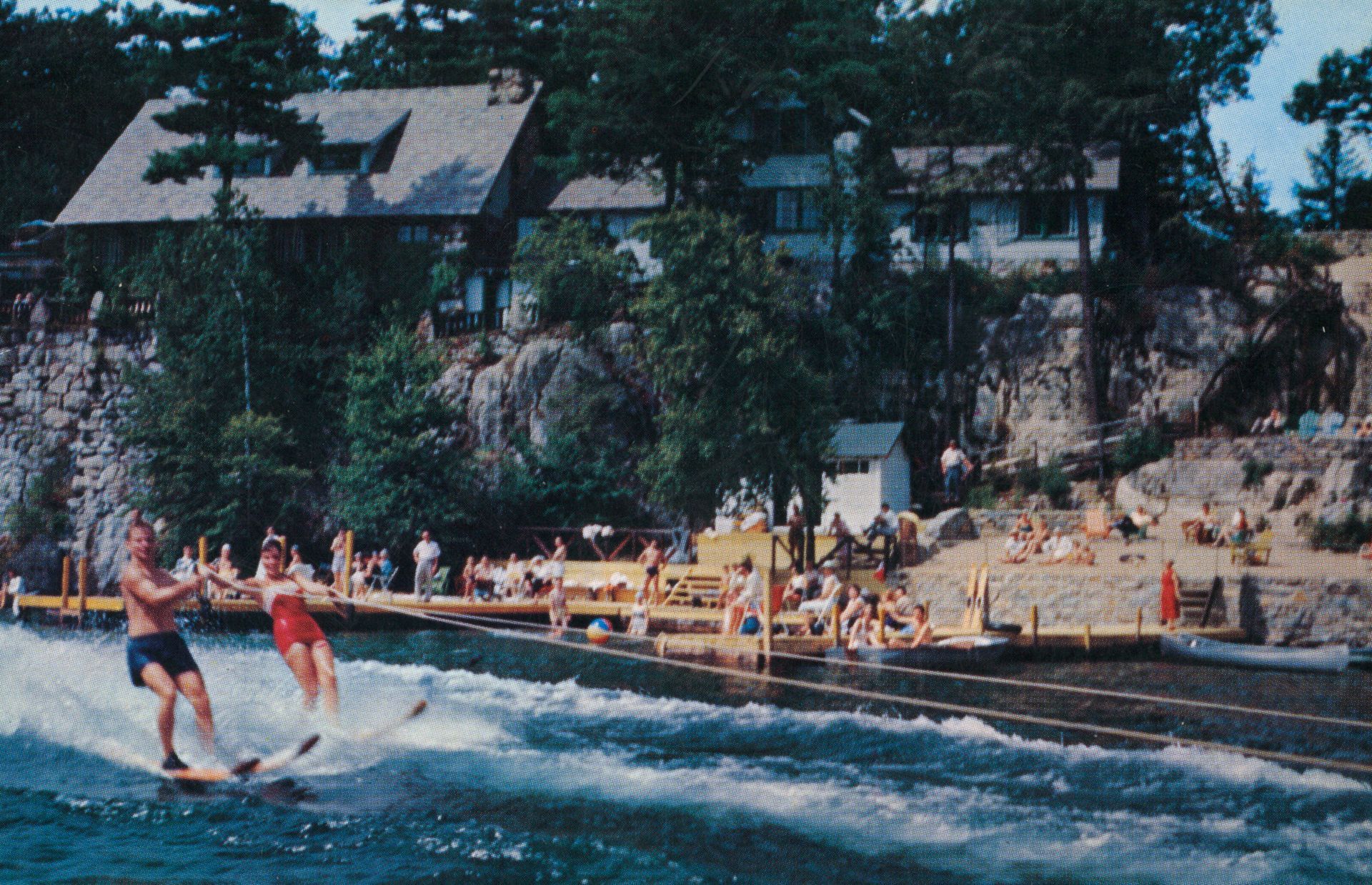 A group of people are water skiing on the lake in front of Blue Water Manor