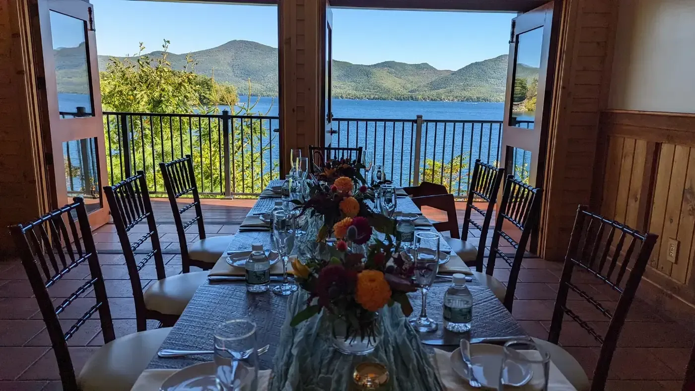A long table with a vase of flowers on it in a room with a view of a lake.