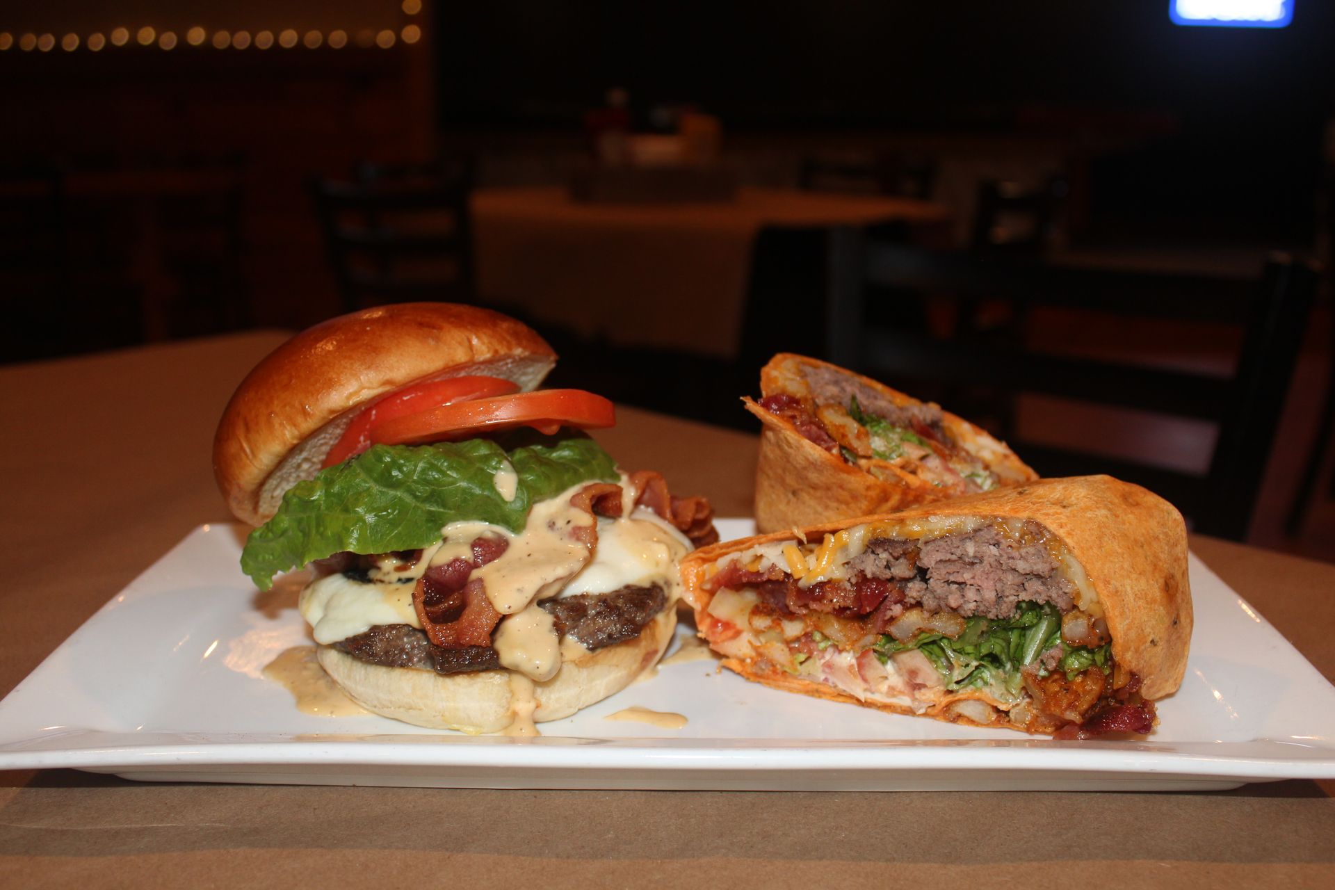 A hamburger and a burrito are on a white plate on a table.