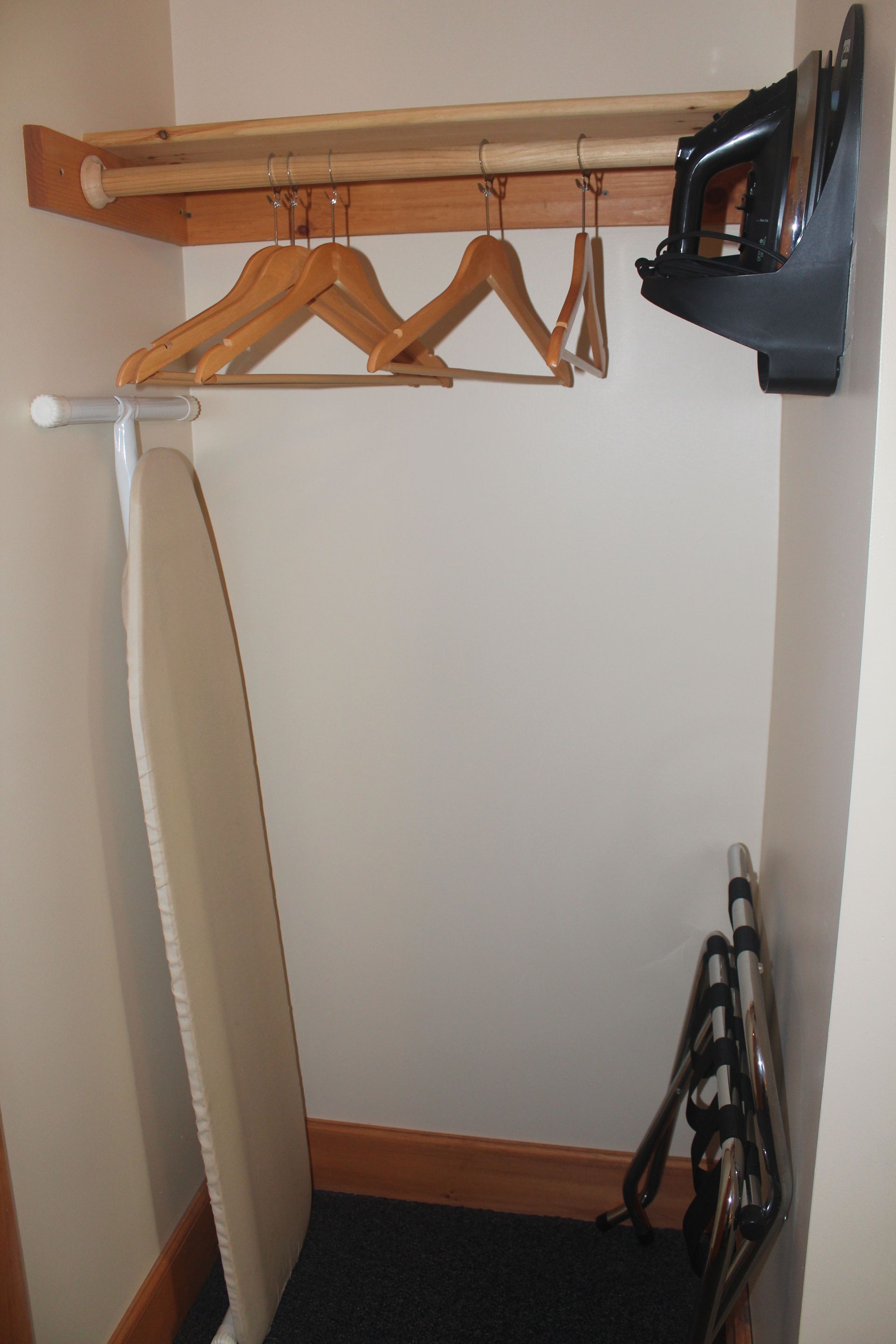 A closet with clothes hanging on a rack and an ironing board