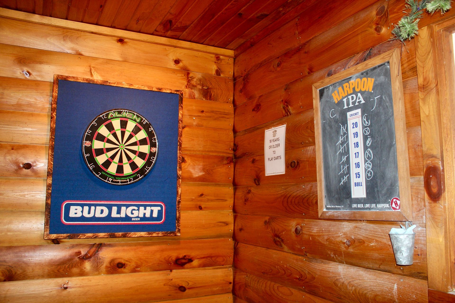 A dart board is hanging on a wooden wall next to a bud light sign.