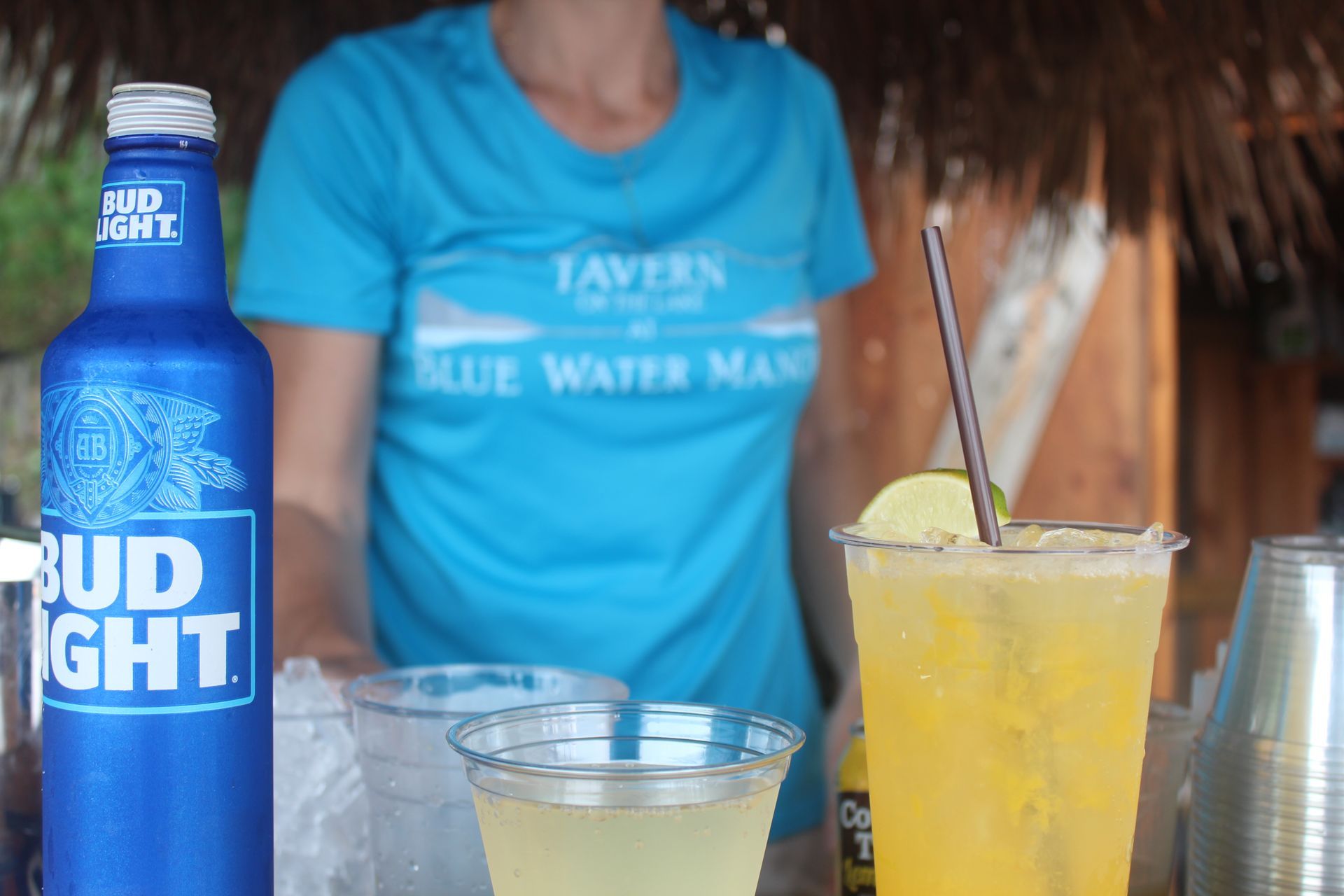 A woman in a blue shirt is standing in front of a bottle of bud light