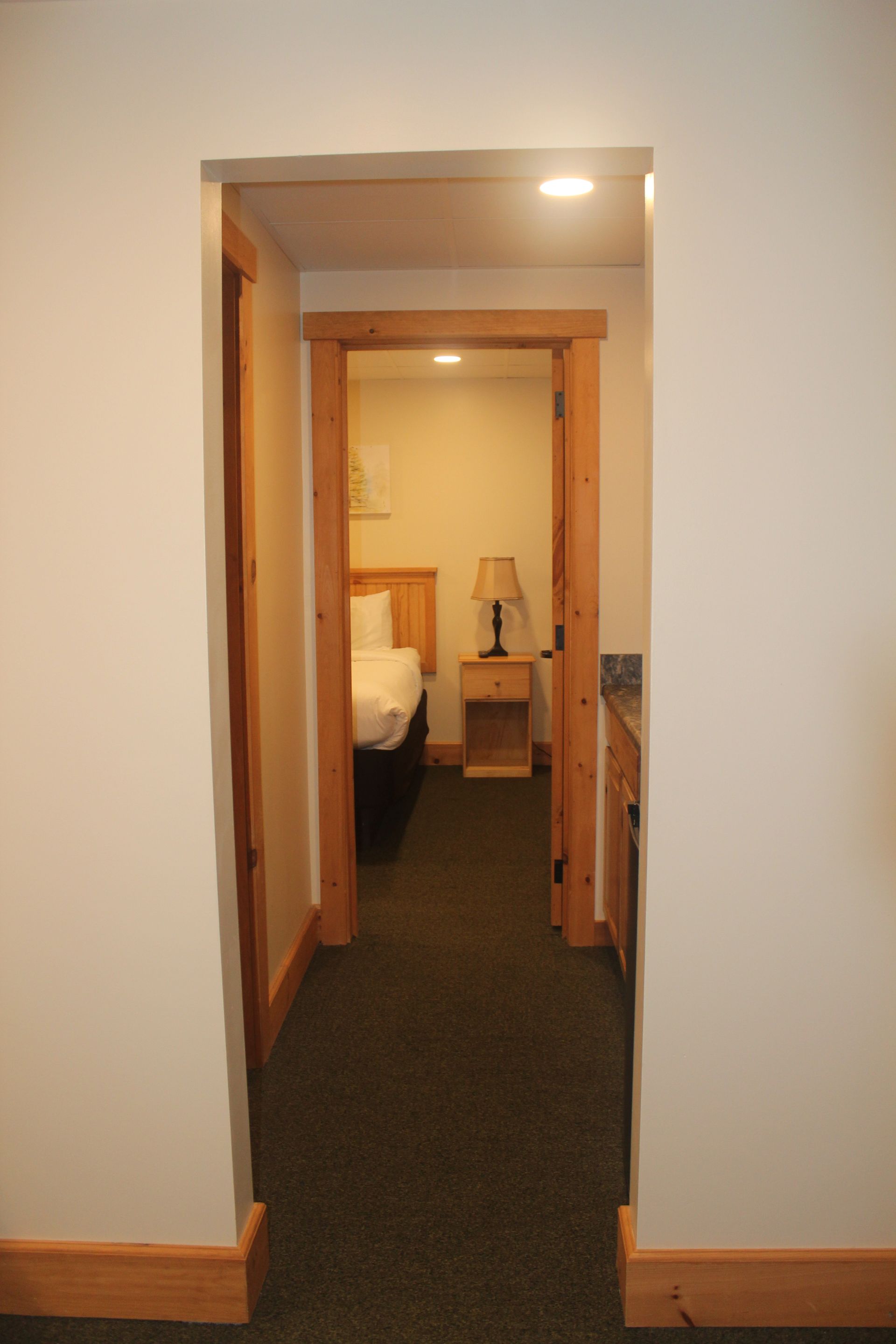 A hallway leading to a bedroom with a bed and nightstand