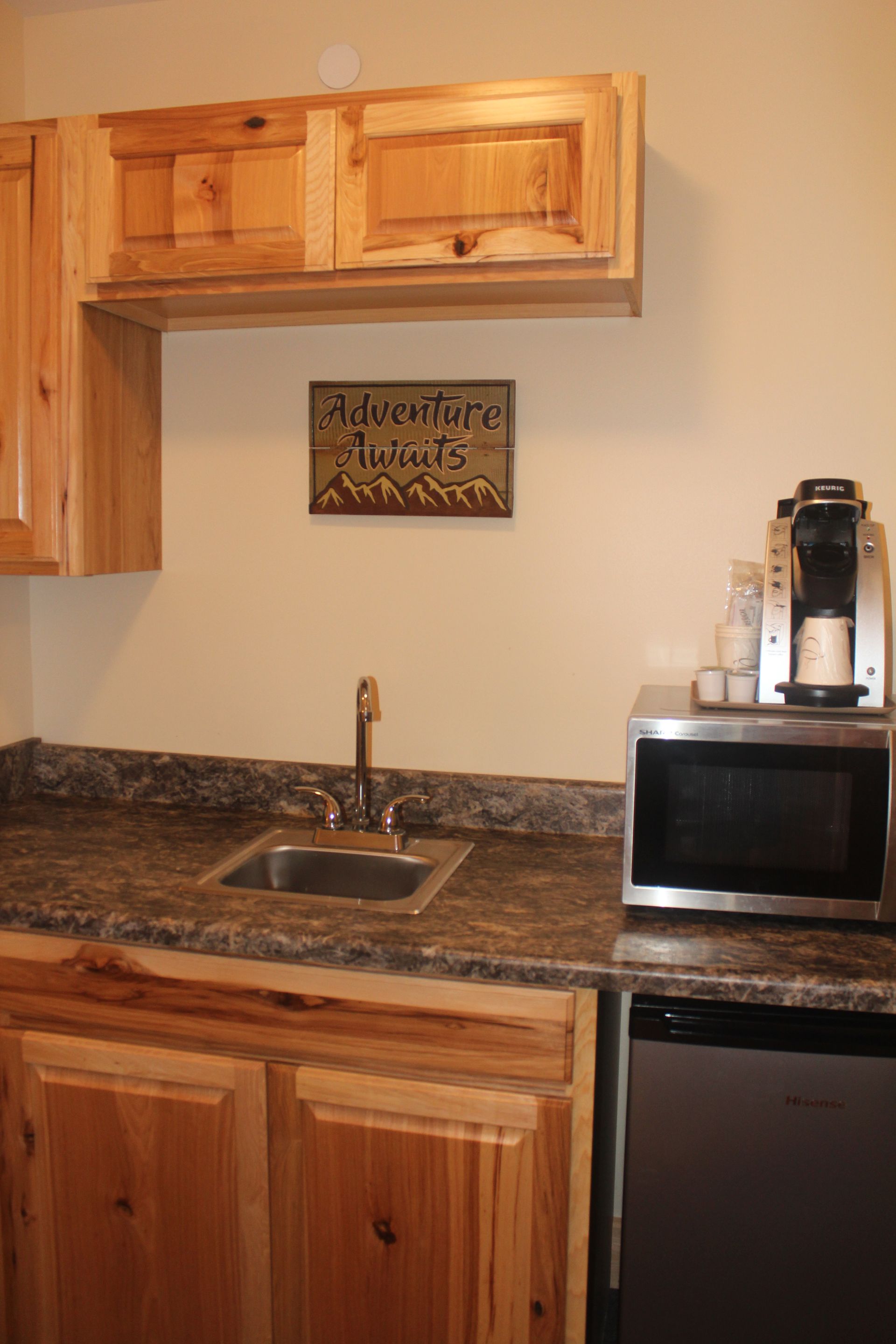 A kitchen with wooden cabinets , a sink , a microwave , and a sign that says adventure tours