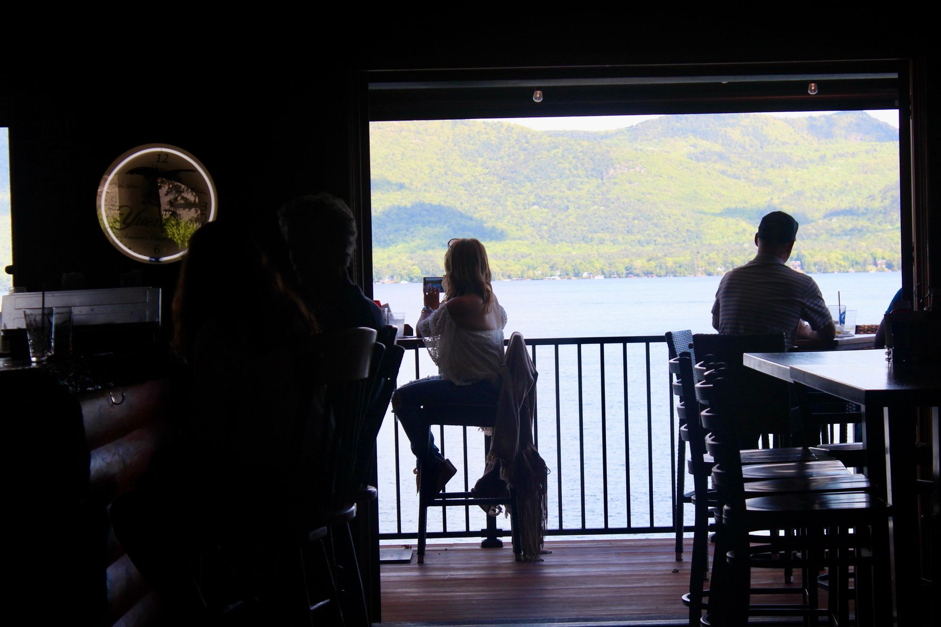A group of people are sitting at tables on a balcony overlooking a lake.