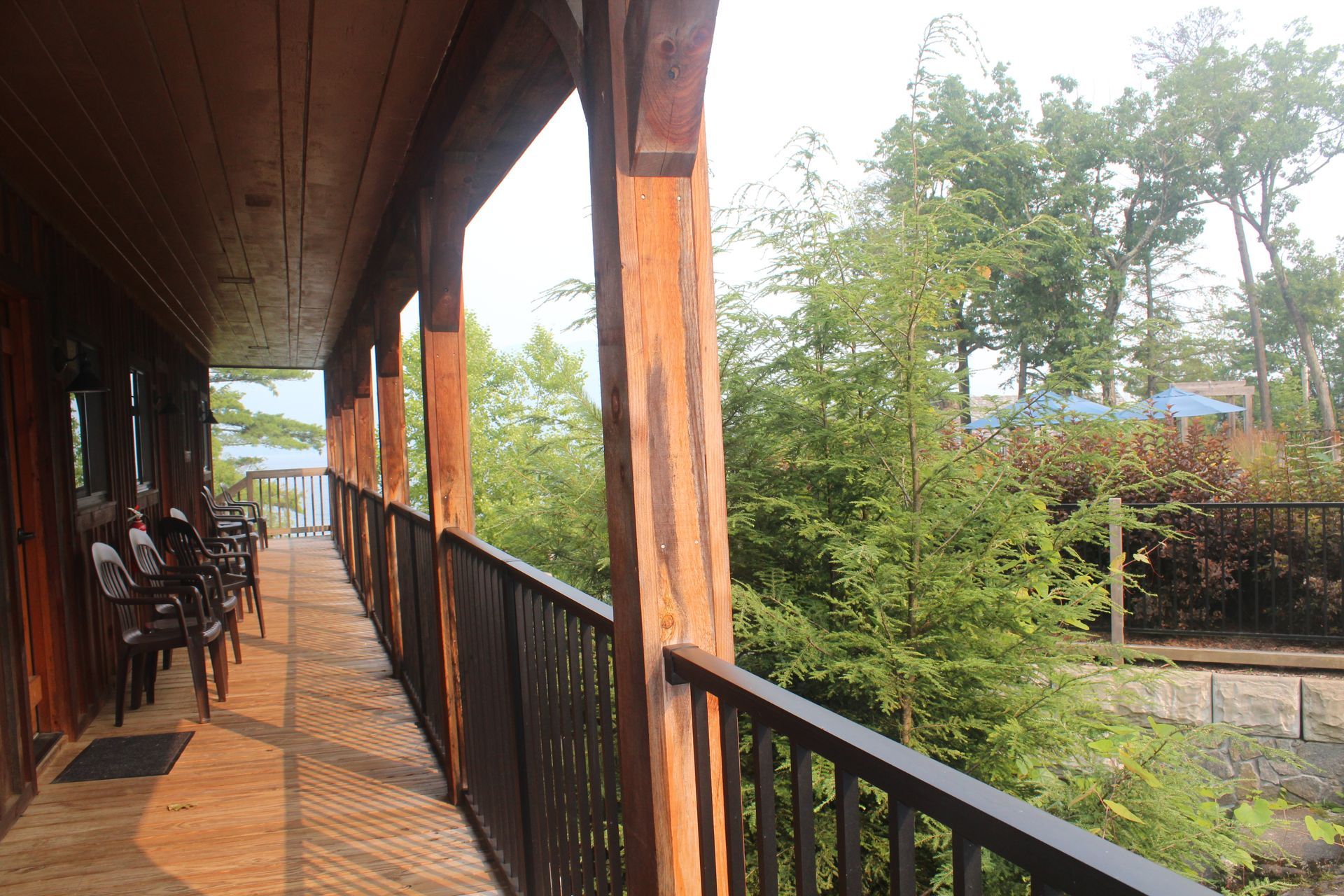A long wooden porch with a black railing and chairs.