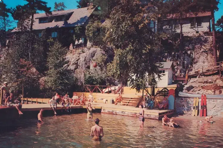 A group of people are swimming in a lake with a house in the background