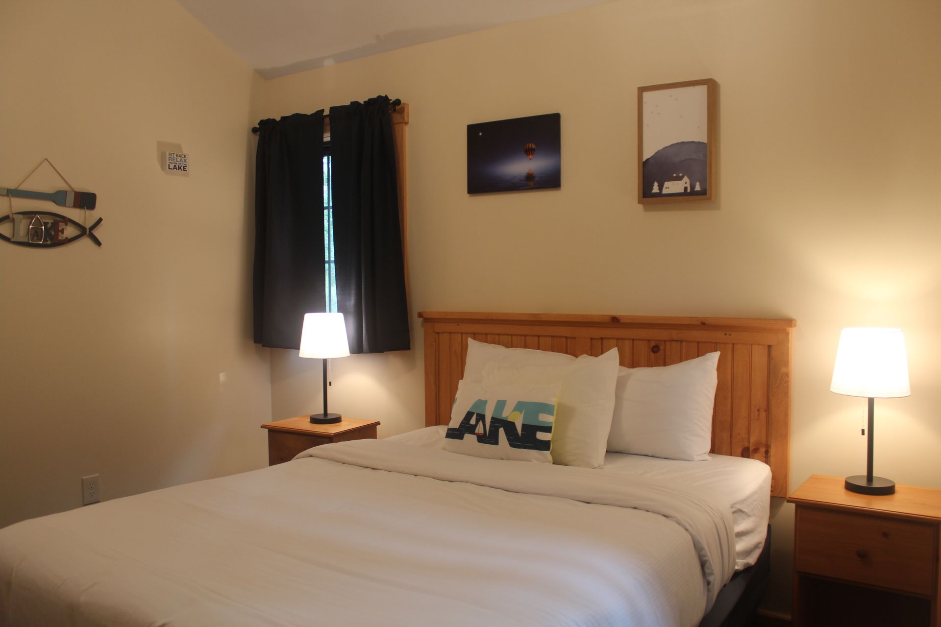A bedroom with a bed , two nightstands , a lamp and a fish on the wall.