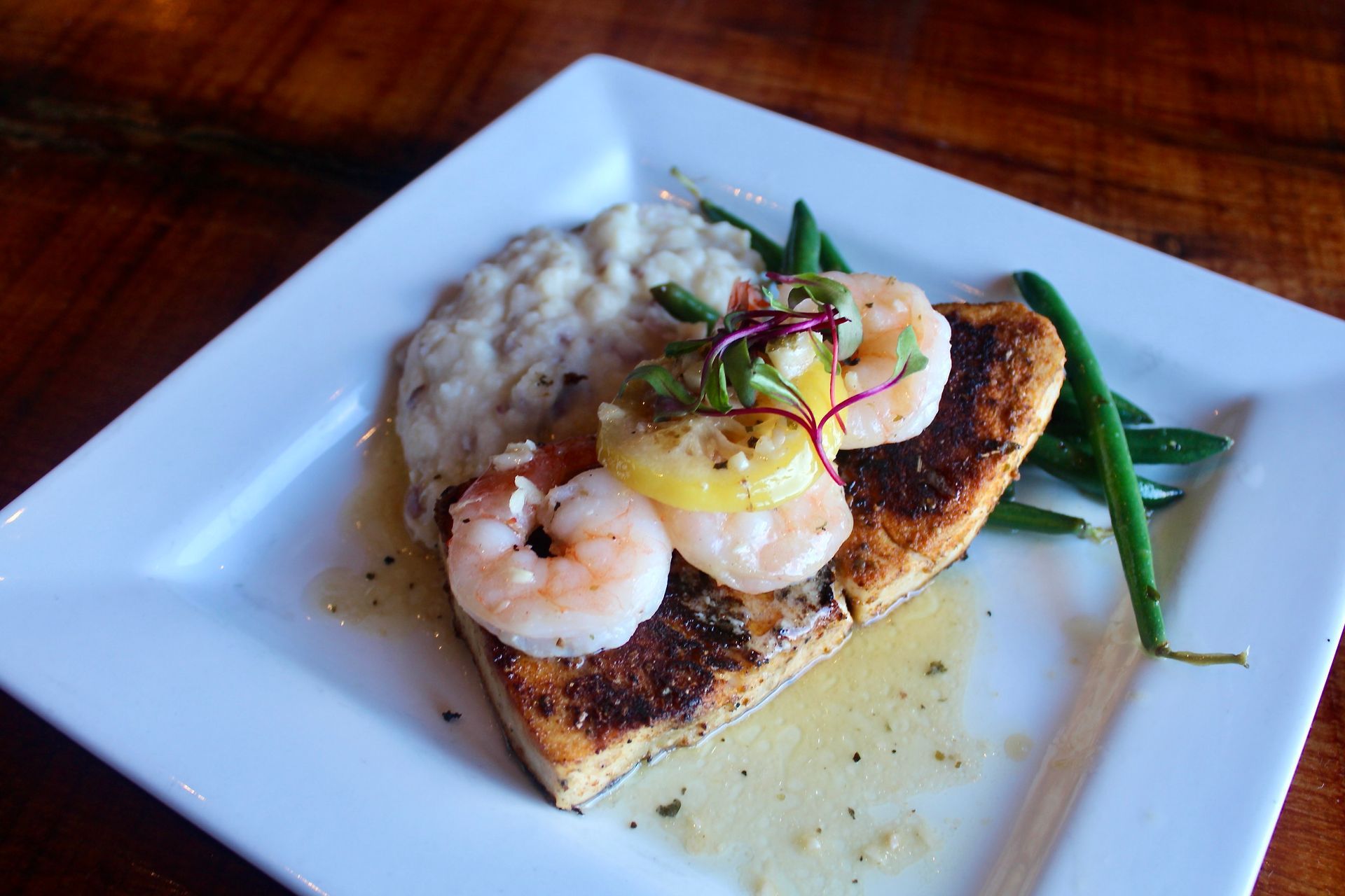 A white plate topped with shrimp and green beans on a wooden table.