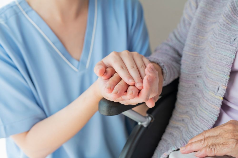 A nurse is holding the hand of an elderly woman in a wheelchair.