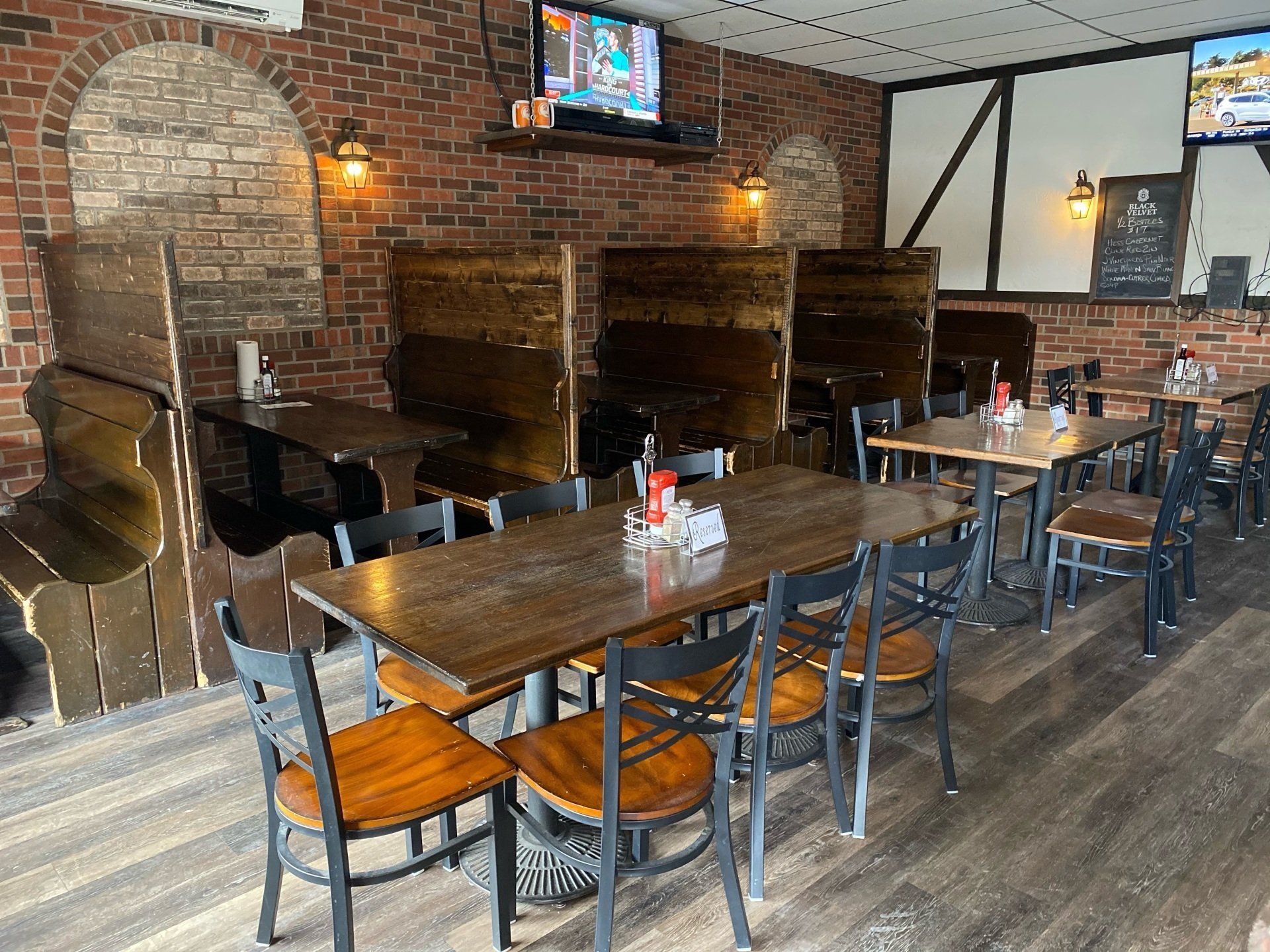 Restaurant interior with wooden booths, tables, chairs, and brick walls. Television mounted on the wall.
